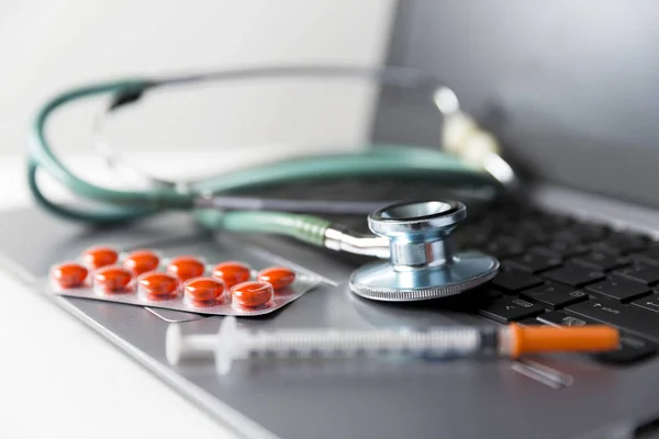 Pack van geneeskunde pillen, spuit en stethoscoop opleggen van laptop — Stockfoto