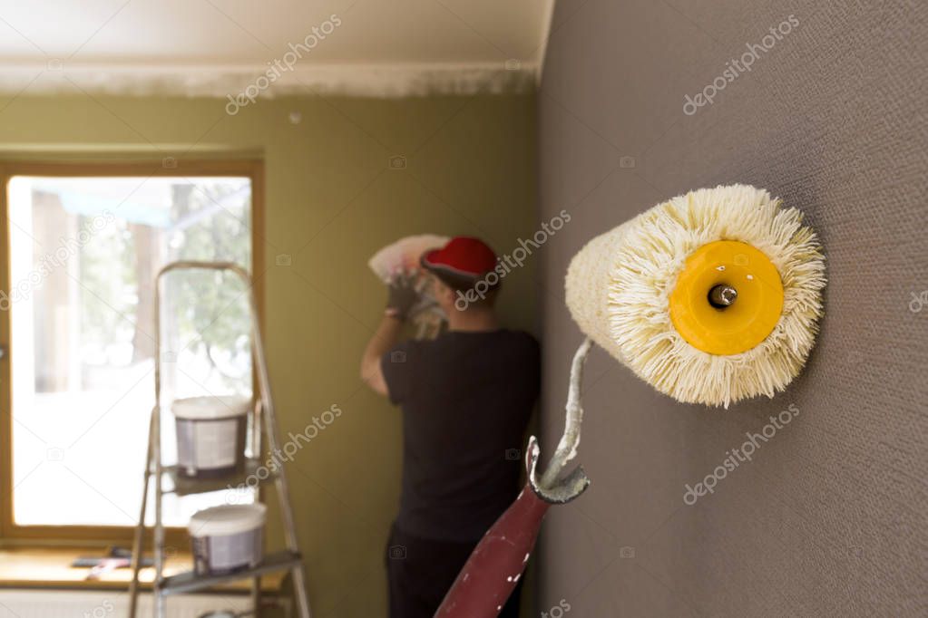 Roller for painting against grey wall. Decorator choosing color 