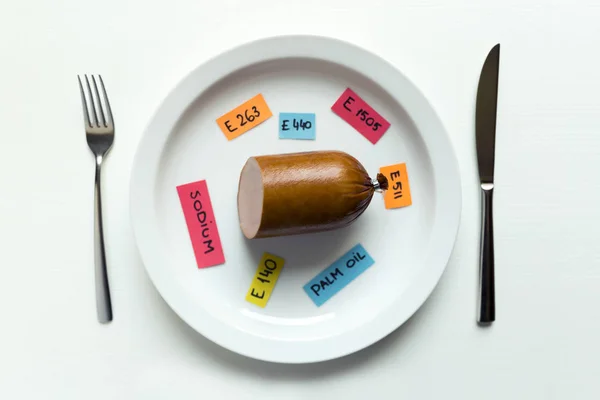 Colorful paper notes naming food additives and sausage on plate with fork and knife, food additive and unhealthy food concept.