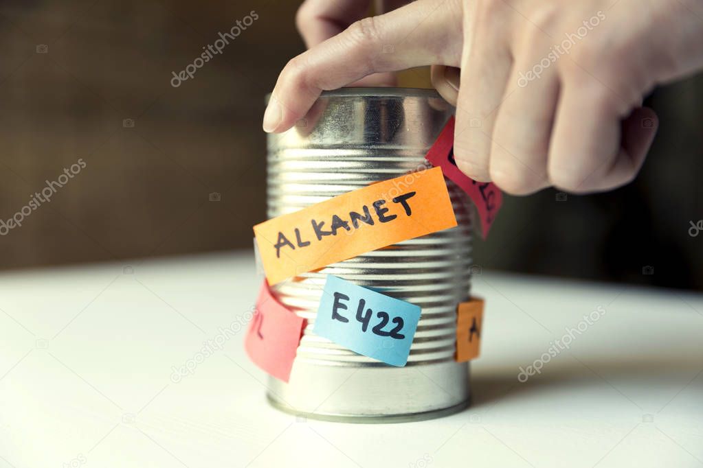Woman's hand opening canned food with paper notes naming food additives. Healthy food concept