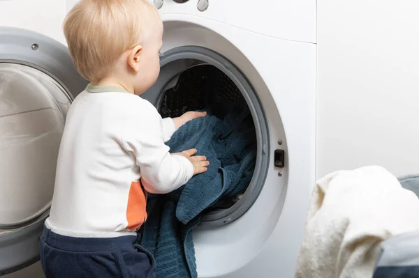 Niño de dos años haciendo tareas domésticas. Carga de máquinas de lavado — Foto de Stock