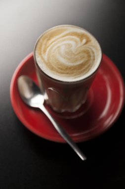 Kırmızı çay tabağında servis edilen harika Latte Macchiato.