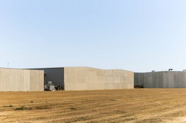 Arka beton duvarda boş arazide toprak üzerinde fabrika var.