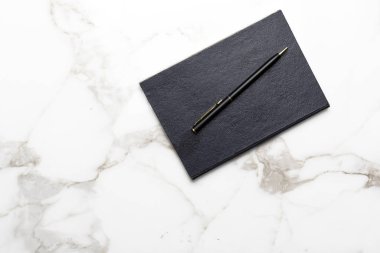 Beyaz mermer yüzeyde siyah kalem & not defteri