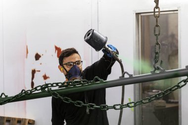Sprey kabin boyacısı metal bar yüzeyine yeşil boya çiziyor.
