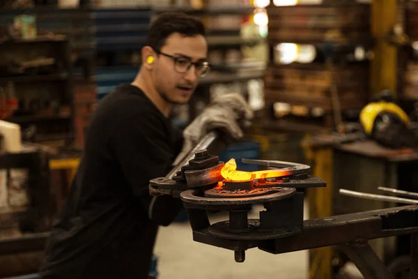 Herrero doblando metal caliente en ambiente de fábrica — Foto de Stock