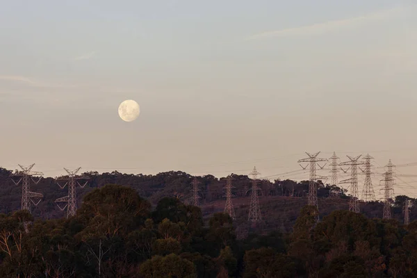 Vollmonduntergang in der Dämmerung über der natürlichen Landschaft unten mit Strommasten — Stockfoto