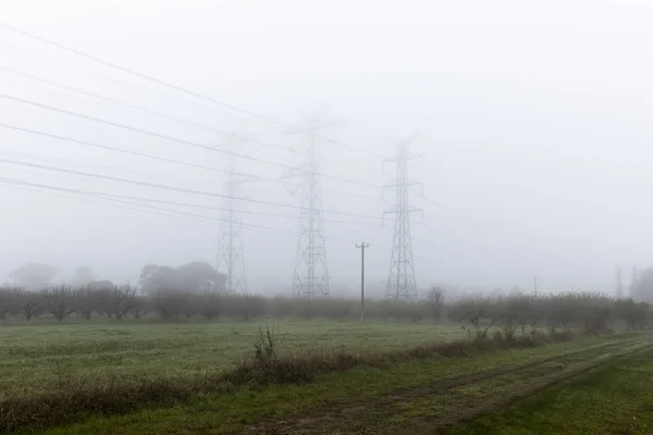 Neblige Landschaft mit Hochspannungsmasten entlang der Landstraße — Stockfoto