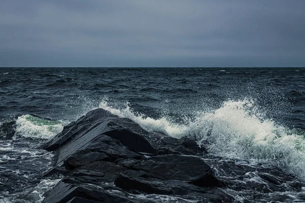 Waves breaking at the shore at the black rocks — Stock Photo, Image