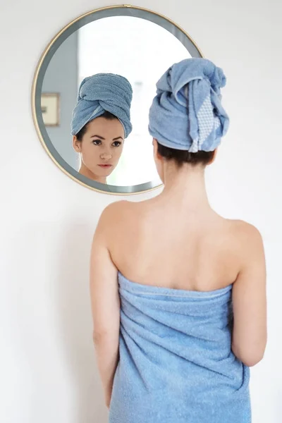 Młoda kobieta zawinięte w ręcznik, patrząc w lustro — Zdjęcie stockowe