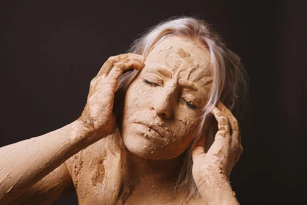 Woman covered in dry cracked clay mud mask holding her head — Stock Photo, Image