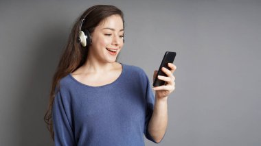 Kulaklıklı, akıllı telefonuyla müzik dinleyen mutlu genç bir kadın.