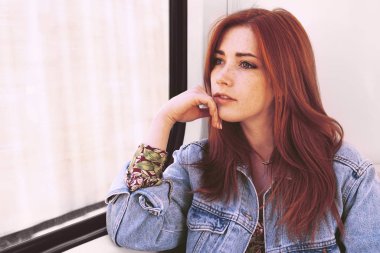 Pencereden dışarı bakan genç bir kadın hayal kuruyor.