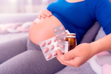 Hamilelik sırasındaki vitaminler. Elinde haplar tutan ve karnını gösteren hamile bir kadın.. 