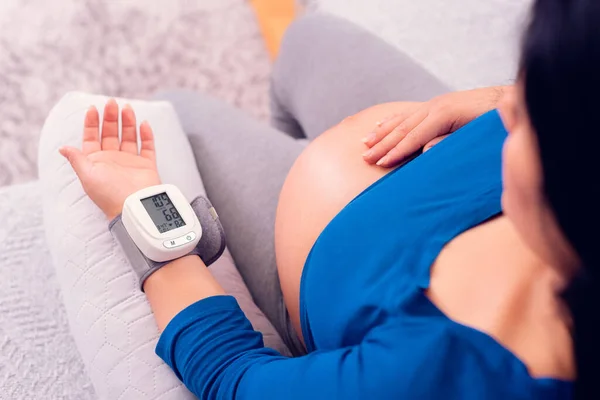 妊娠中の女性は彼女の手首の医療機器と自宅で血圧を監視し 彼女の腹を公開 — ストック写真
