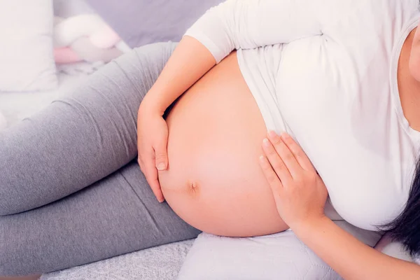 妊娠中の女性がソファに座って妊娠中の赤ん坊を抱えてる 母なる時 — ストック写真