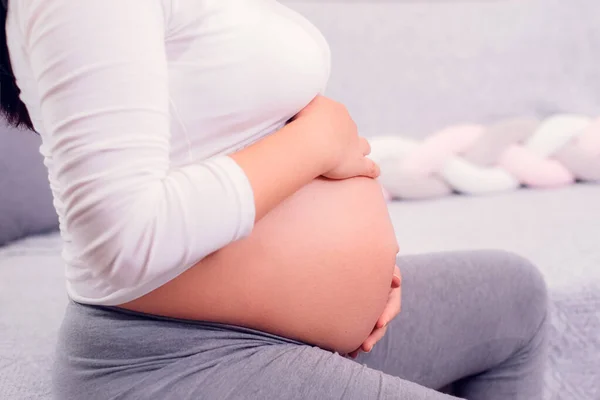 妊娠中の女性がソファに座って妊娠中の赤ん坊を抱えてる 母なる時 — ストック写真