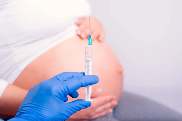 妊娠中の女性は注射を受けてる 妊娠中の腹の前に青い手袋保持注射器と手 — ストック写真