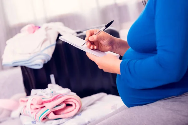 Mujer Embarazada Haciendo Lista Verificación Mientras Empaca Maleta Con Ropa Fotos De Stock