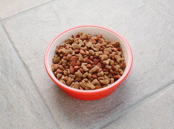Ciotola rossa di cibo secco per gatti su piastrelle grigie — Foto Stock