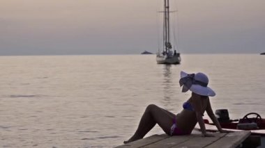 Bikini kadın siluet şapka ve gün batımında yelkenli yat