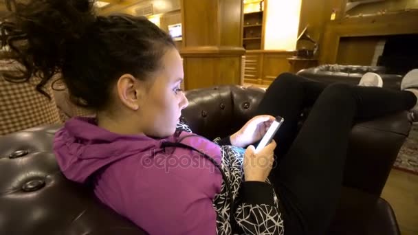 女孩使用智能手机坐在沙发上的酒店 — 图库视频影像