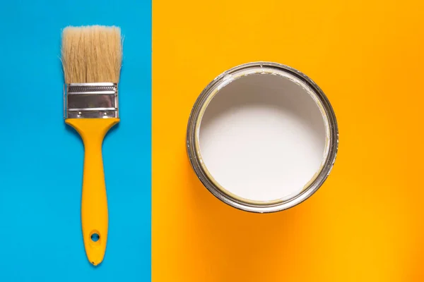 Cepillo y lata de pintura sobre fondo azul amarillo — Foto de Stock