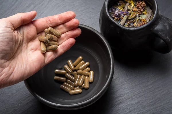 Herbal capsules  in woman hand black stone background