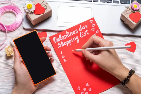 Alla hjärtans dag inköpslista och smart phone på trä skrivbord — Stockfoto
