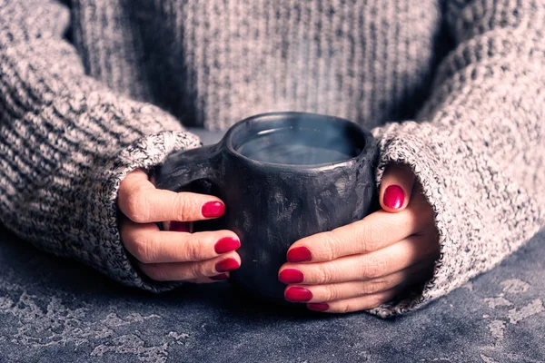 Female hands warm up hands on a hot cup