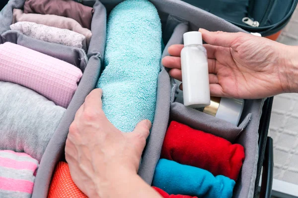 Manos de mujer poniendo toalla y botella de champú de viaje a la maleta , — Foto de Stock