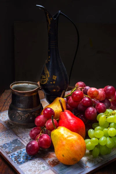 Starožitný kovový džbán, hrozny a hrušky na dřevěný stůl — Stock fotografie