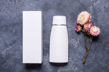 Gri arkaplanda krema şişesi ve karton kutu var.