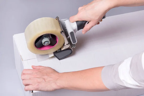 Worker works with tape dispenser, closing cardboard industrial box