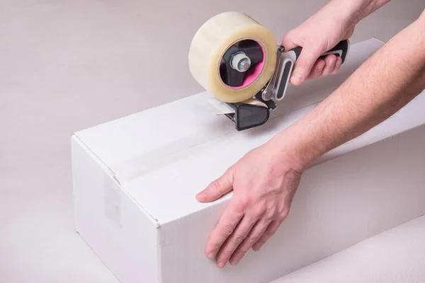 Worker works with tape dispenser, closing cardboard industrial box