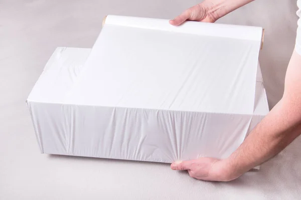 Csomagoló kartondoboz fehér raklapos fóliával, dolgozó kezekkel — Stock Fotó