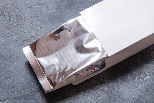 Koyu gri arkaplanda folyo paketi ve beyaz karton kutu — Stok fotoğraf