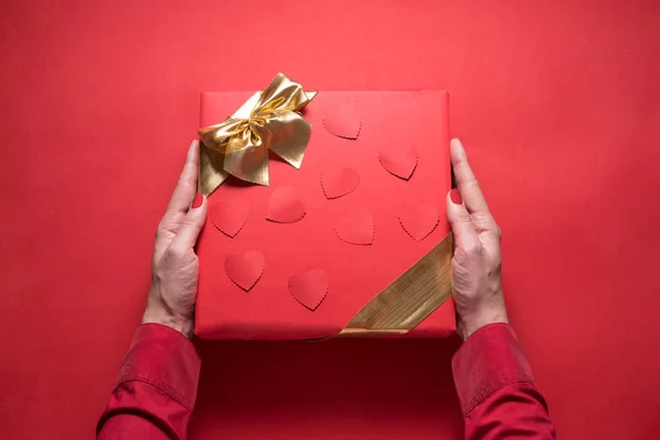 Woman hands holding red gift box with gold ribbon on red backgro