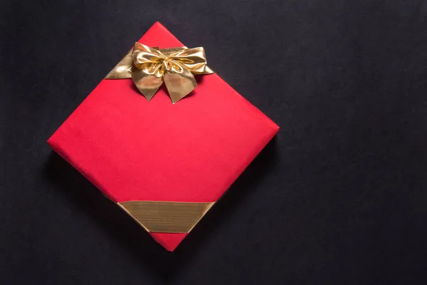 Red gift box with gold ribbon on black background, copy space