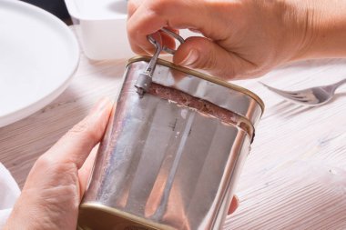 Kadın elleri konserve kutusunu konserve sığır etiyle açıyor, mutfak masasının üstünde.