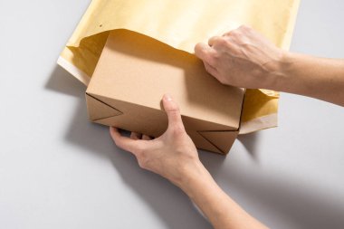 Kadın elleri büyük bir posta zarfının içine karton kutu koyuyor.