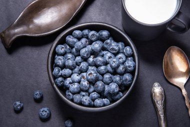 Siyah seramik kasede taze yabanmersini ve bir fincan süt.