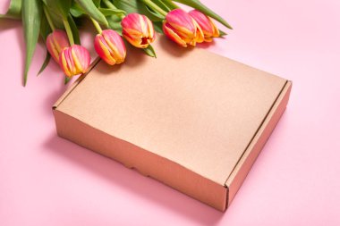 Kahverengi karton kutu ve pembe arka planda lale çiçekleri