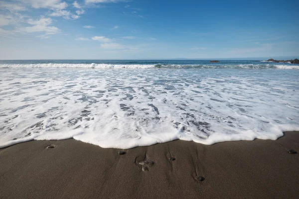 Vatten skum i vulkanisk sand beach i La Gomera, Kanarieöarna, Spanien. — Stockfoto