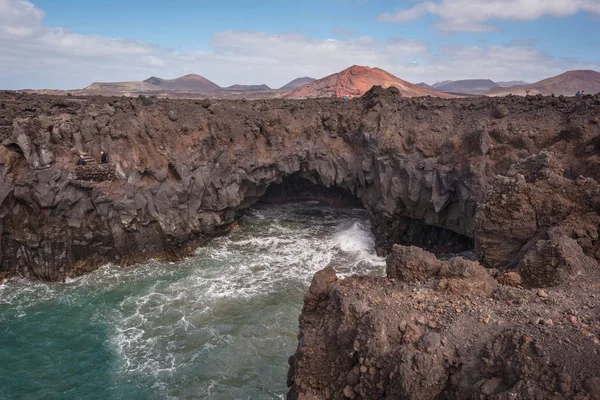 Lanzarote paisaje. Costa de Los Hervideros, cuevas de lava, acantilados y océano ondulado. Turista no identificable están en el fondo — Foto de Stock