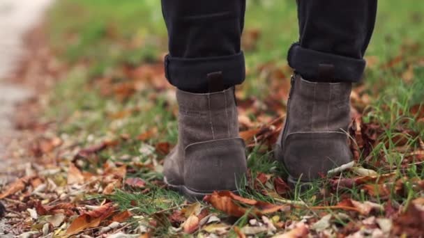 Mladý muž v kožených botách kráčí po pěšině s spadlým listím. Podzimní sezóna. Outdoor city walk concept slow motion. — Stock video