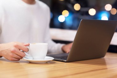 Kafede dizüstü bilgisayarı ve kahve fincanı olan adama yaklaş..