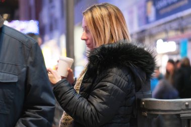Akıllı telefonu ve kahvesi olan güzel genç bir kadın şehirde mutlu bir şekilde gülümsüyor..