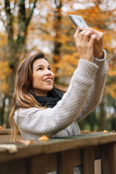 Mulher feliz jovem bonita levando selfie com smartphone no parque de outono. Temporada, tecnologia e conceito de pessoas . — Fotografia de Stock