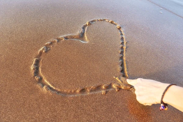 Femme dessinant un cœur sur le sable au coucher du soleil dans un concept d'amour d'été . — Photo